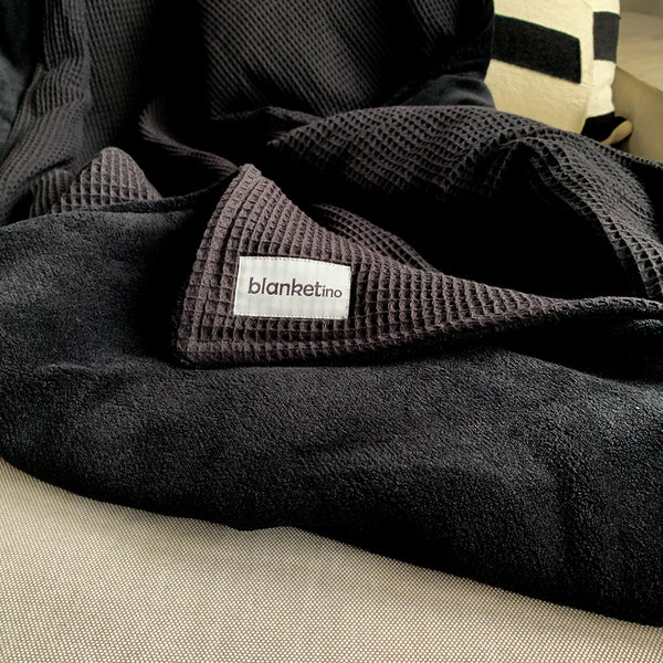 Kuschelige Decke von Blanketino in schwarz, sehr groß auf dem Sofa.